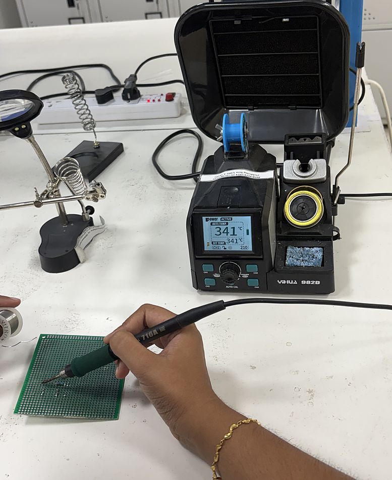 Close view of two hands soldering a component onto a perforated prototyping board.