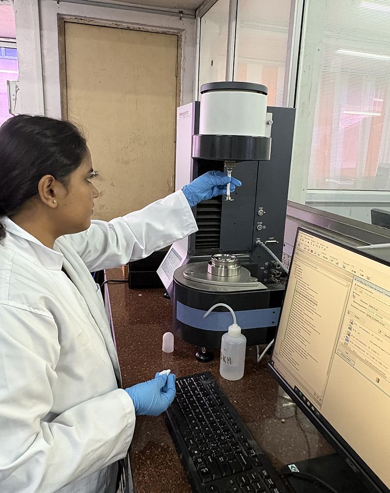 A researcher in a lab coat fitting the measuring geometry onto the spindle of a rotational rheometer.
